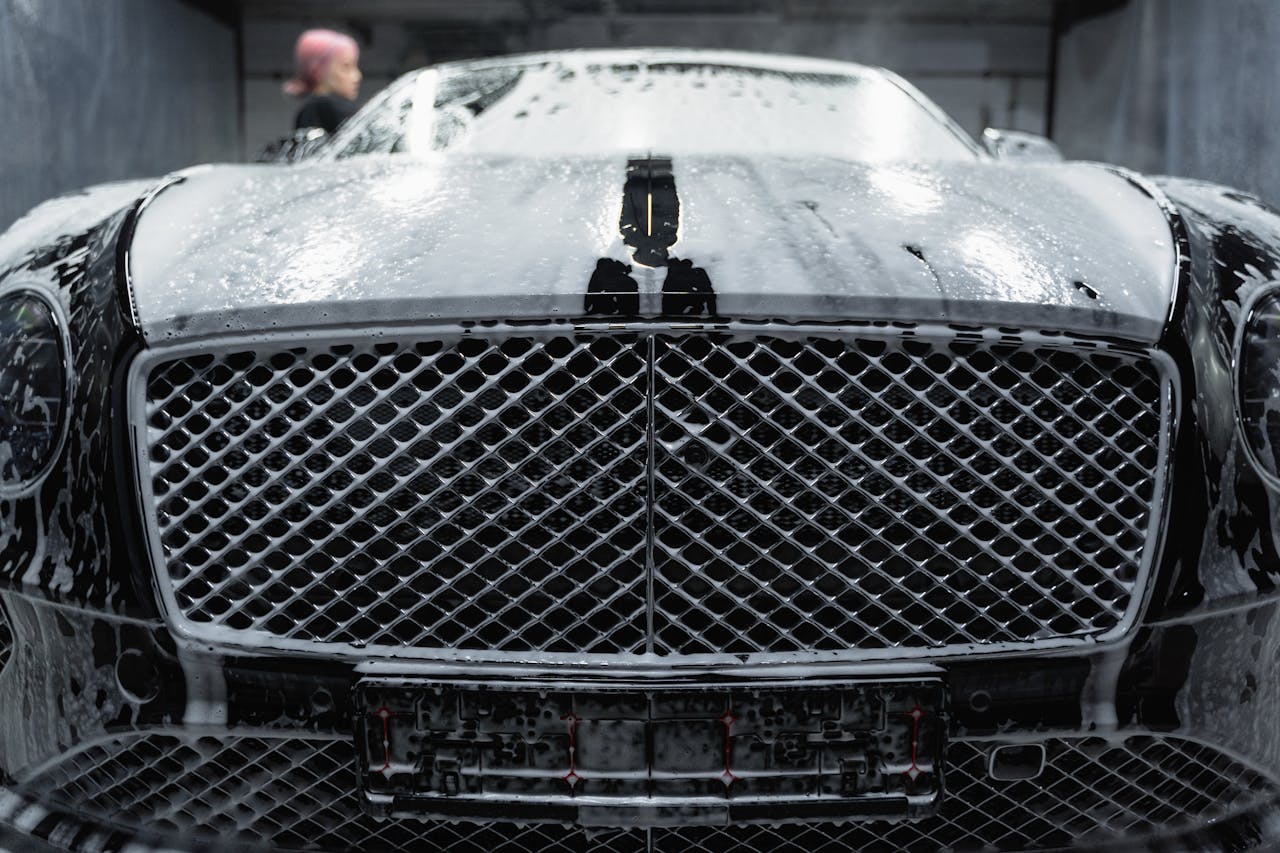 A close-up of a luxurious black car being cleaned with foamy soap at a carwash.