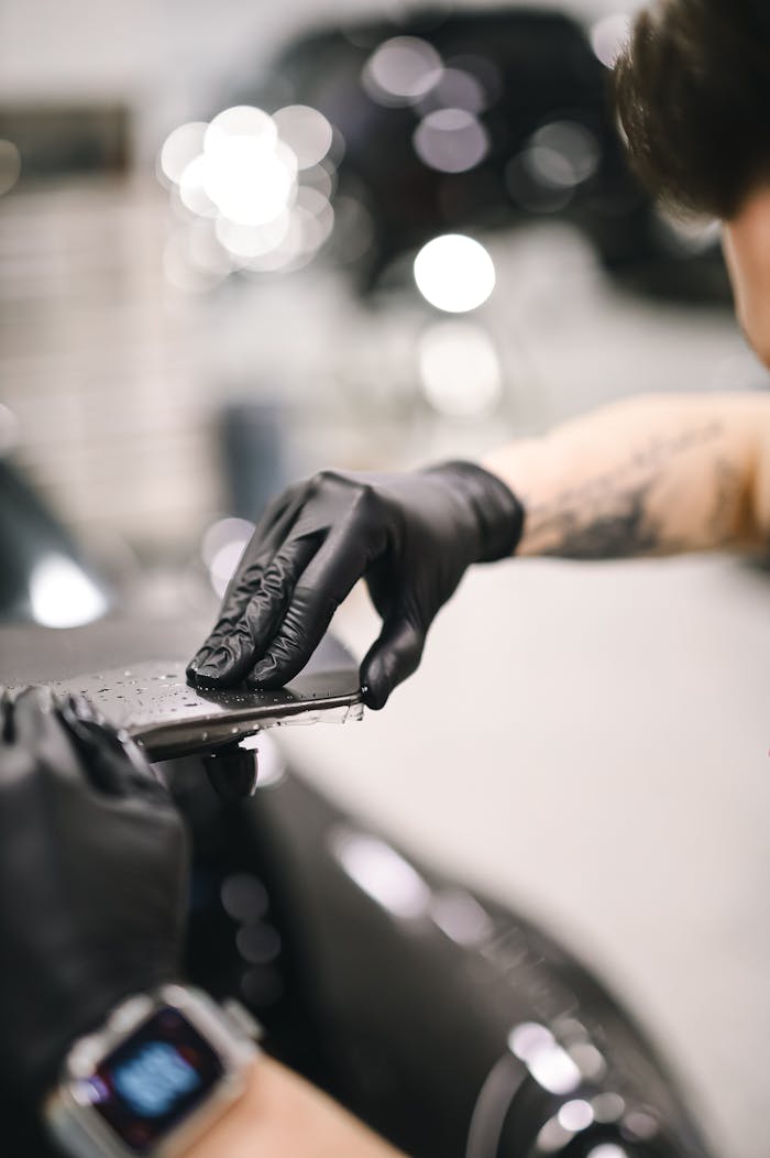 Mechanic uses black gloves for detailing a car in a garage setting.
